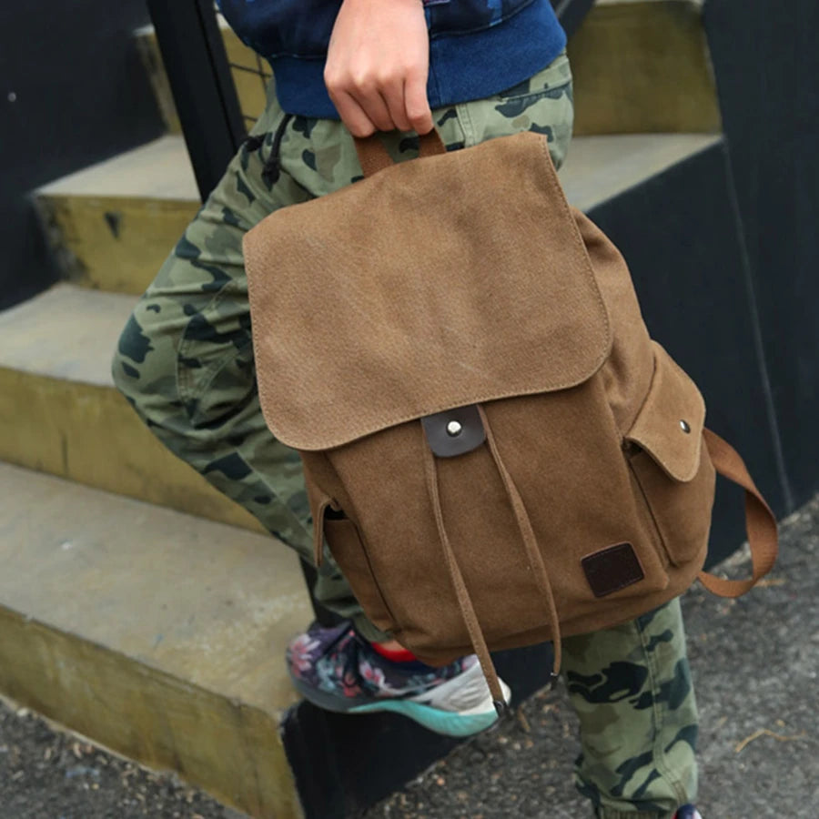 Person holding Orin & Vale brown canvas backpack, wearing camo pants and sneakers on steps